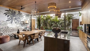 Una cocina moderna con una isla grande, techo de madera y vistas a un jardín exuberante y una piscina.