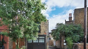 Une ruelle étroite bordée d’immeubles en briques, avec une porte en bois et des plantes en pot.