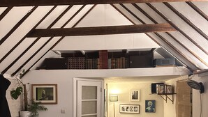Une chambre mansardée chaleureuse avec un lit en mezzanine, des poutres apparentes, un petit bureau et une bibliothèque.