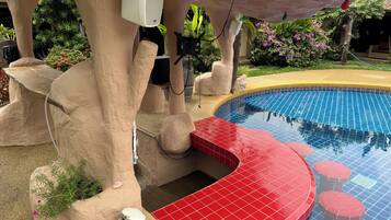 A pool area with a tiled edge, a statue, and a speaker mounted on a rock structure.