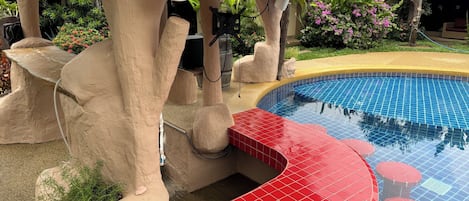 A pool area with a tiled edge, a statue, and a speaker mounted on a rock structure.