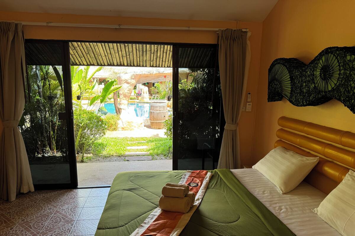 A hotel room with a bed, a view of a pool and garden, and a sliding door.