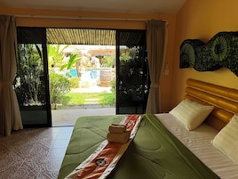 Habitación de hotel con cama, vista a una piscina y jardín, y una puerta corredera.