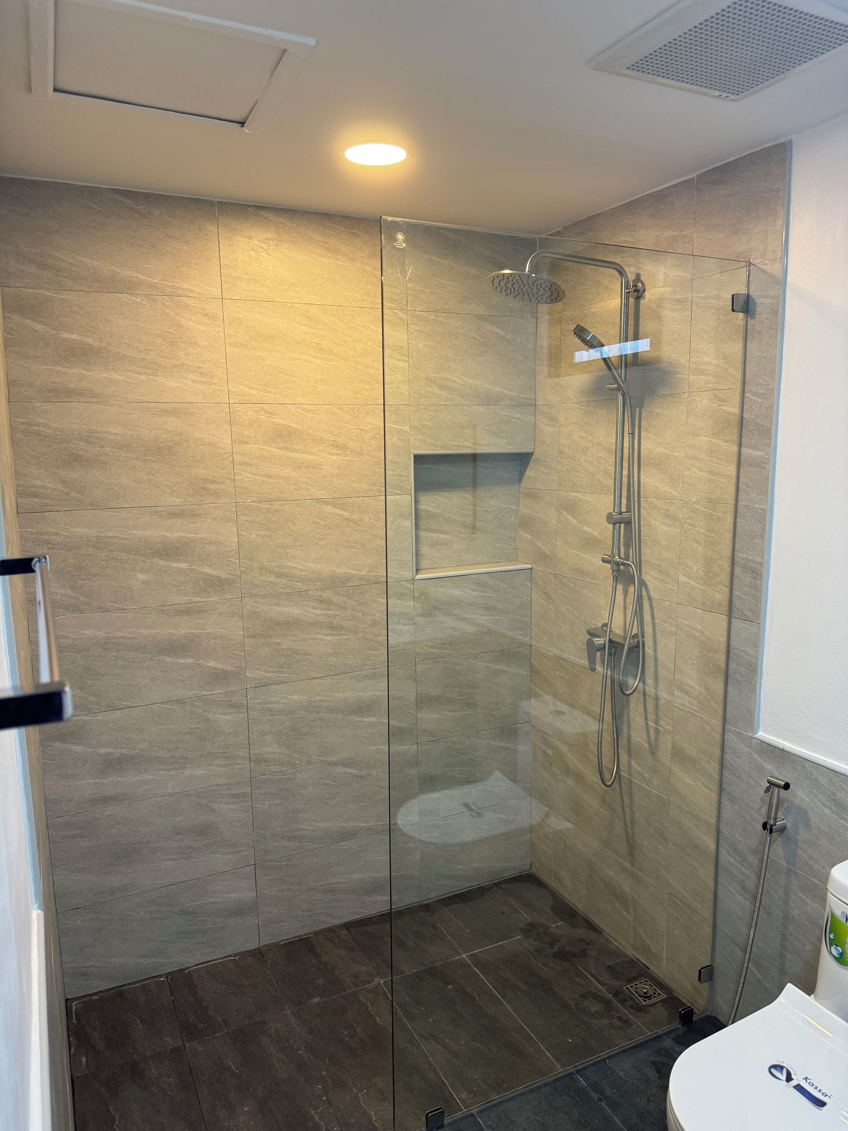 Un baño moderno con ducha envuelta en vidrio, puerta de ducha de cristal y un inodoro con el logotipo de la marca visible.