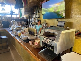 Zona de bar con una pantalla grande mostrando un paisaje pintoresco, una estación de parrilla y varios utensilios y condimentos.