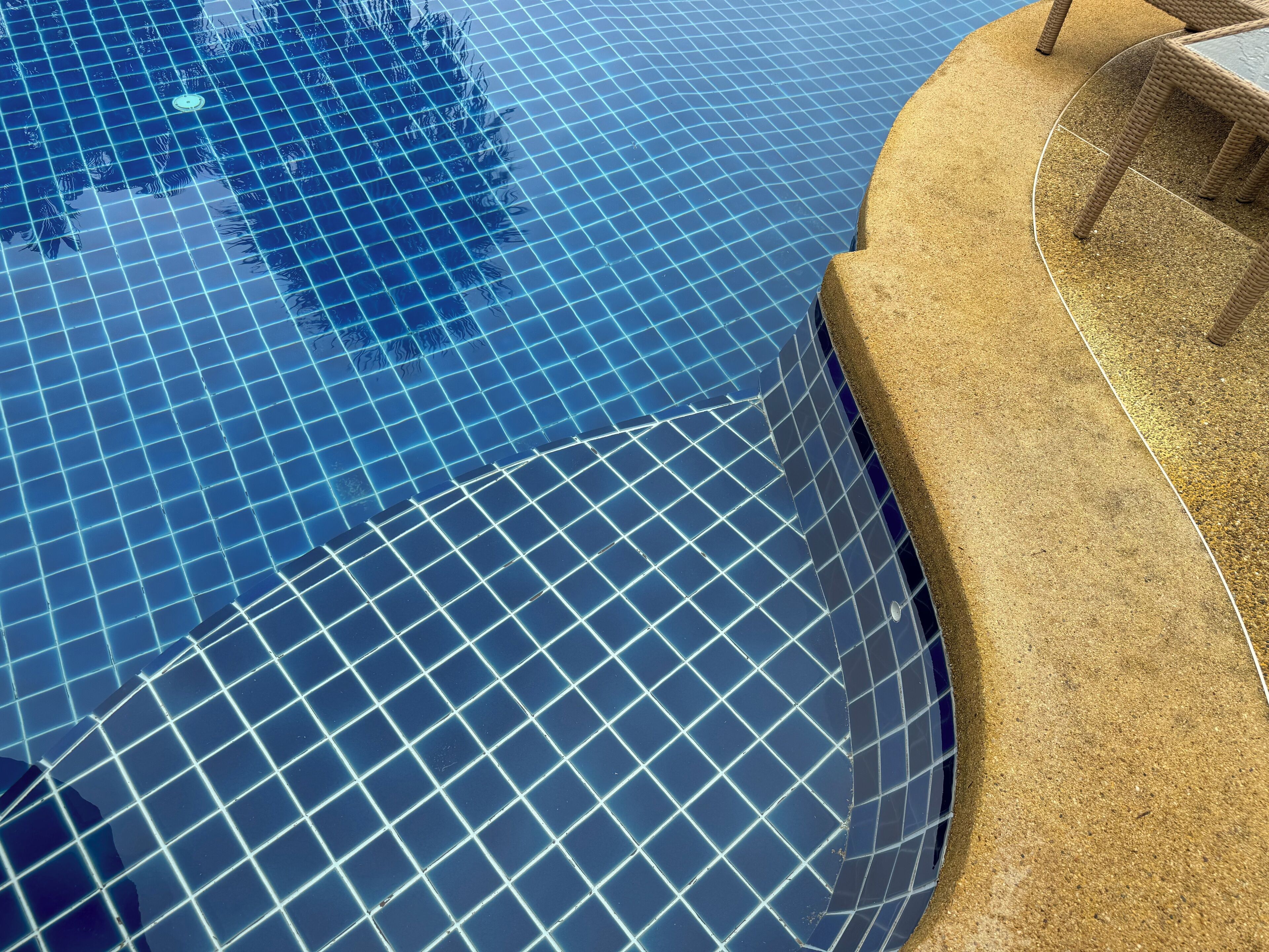A swimming pool with a grid pattern on the surface, surrounded by a textured stone border.