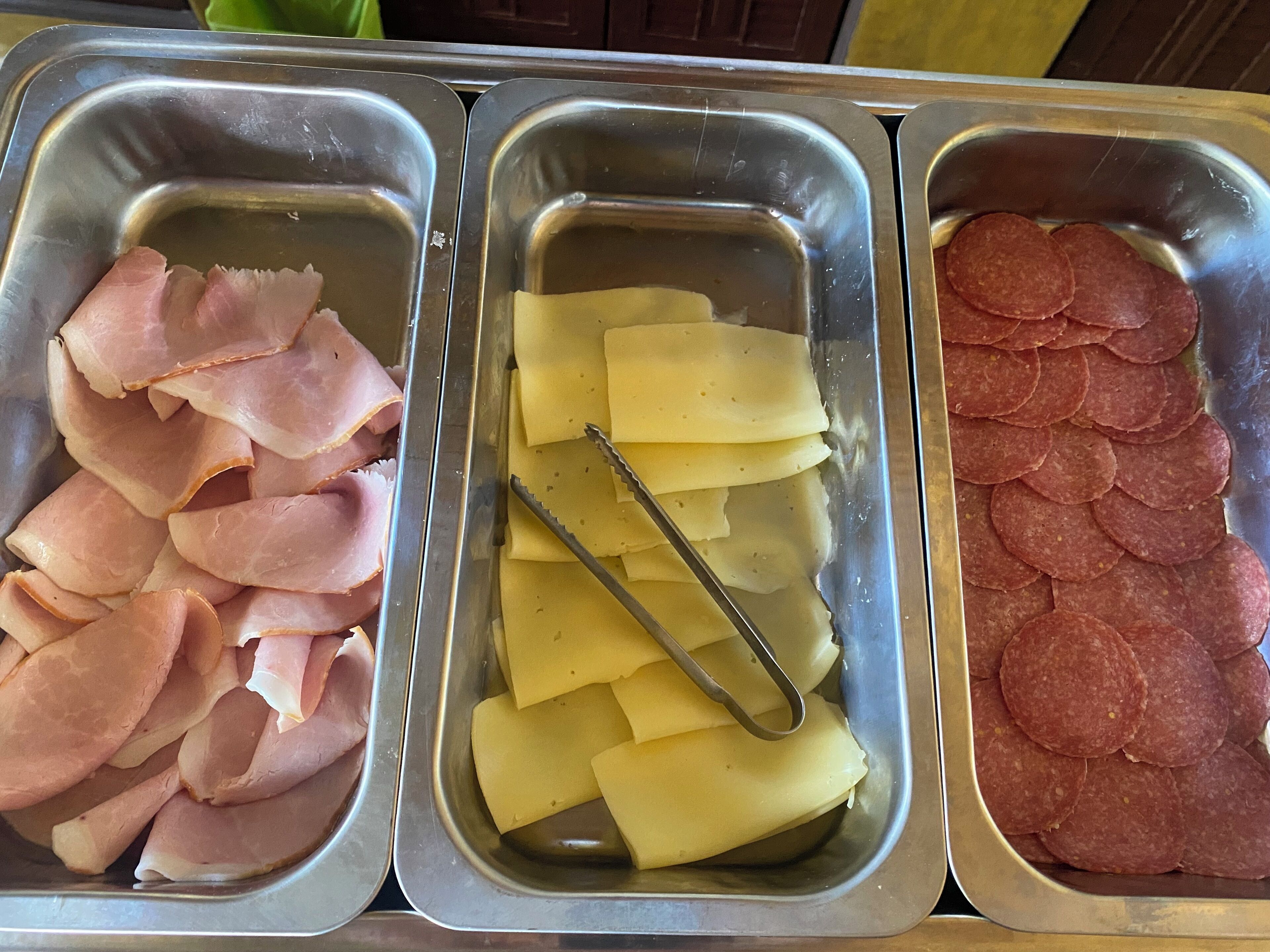 Tres bandejas de metal con jamón en rodajas, queso y pepperoni.