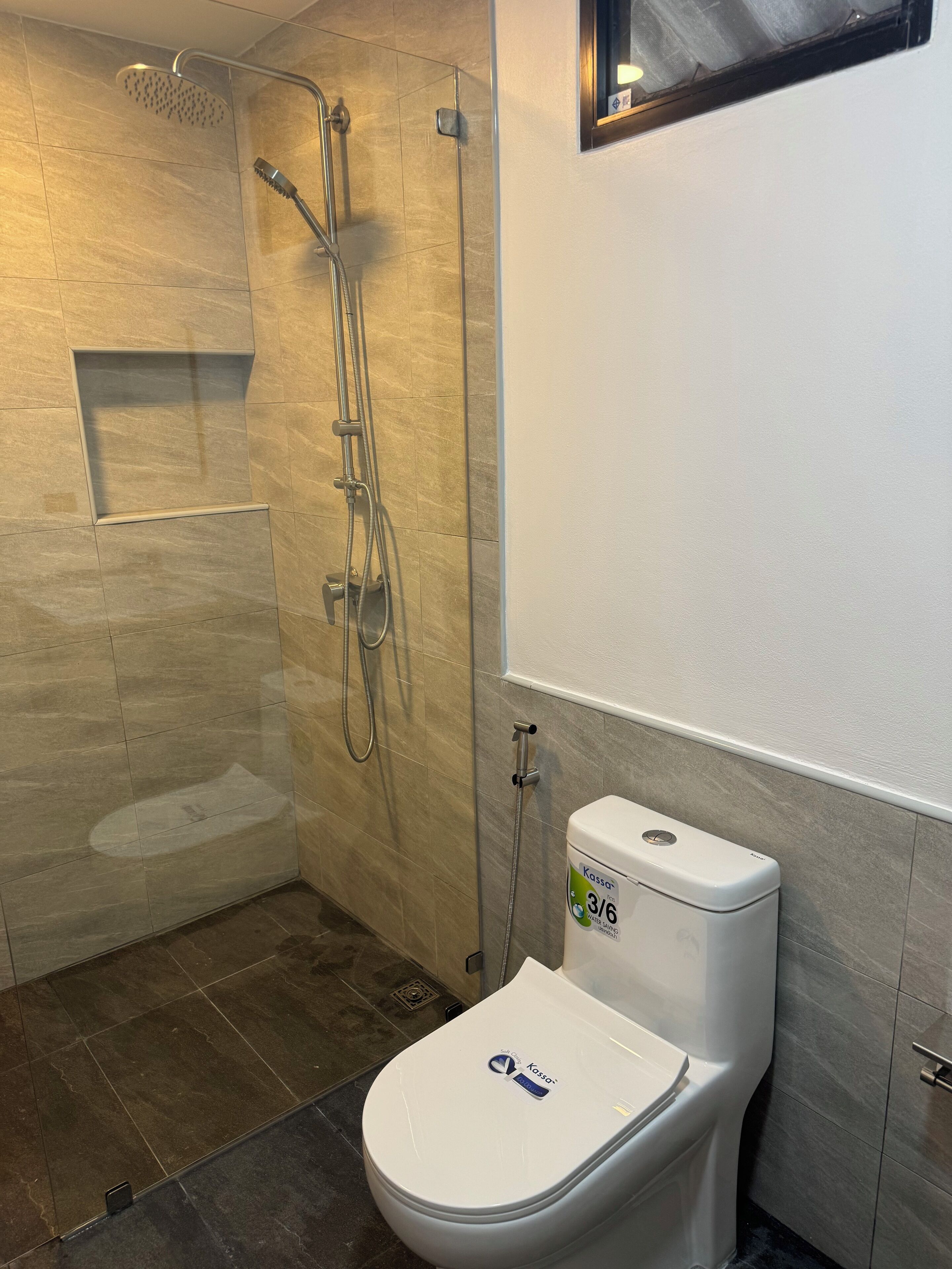 A modern bathroom with a shower, toilet, and a small window.
