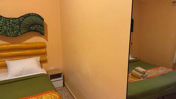 A room with two beds, a green bedspread, a white pillow, a wooden headboard, a small nightstand, and a wall-mounted mirror.