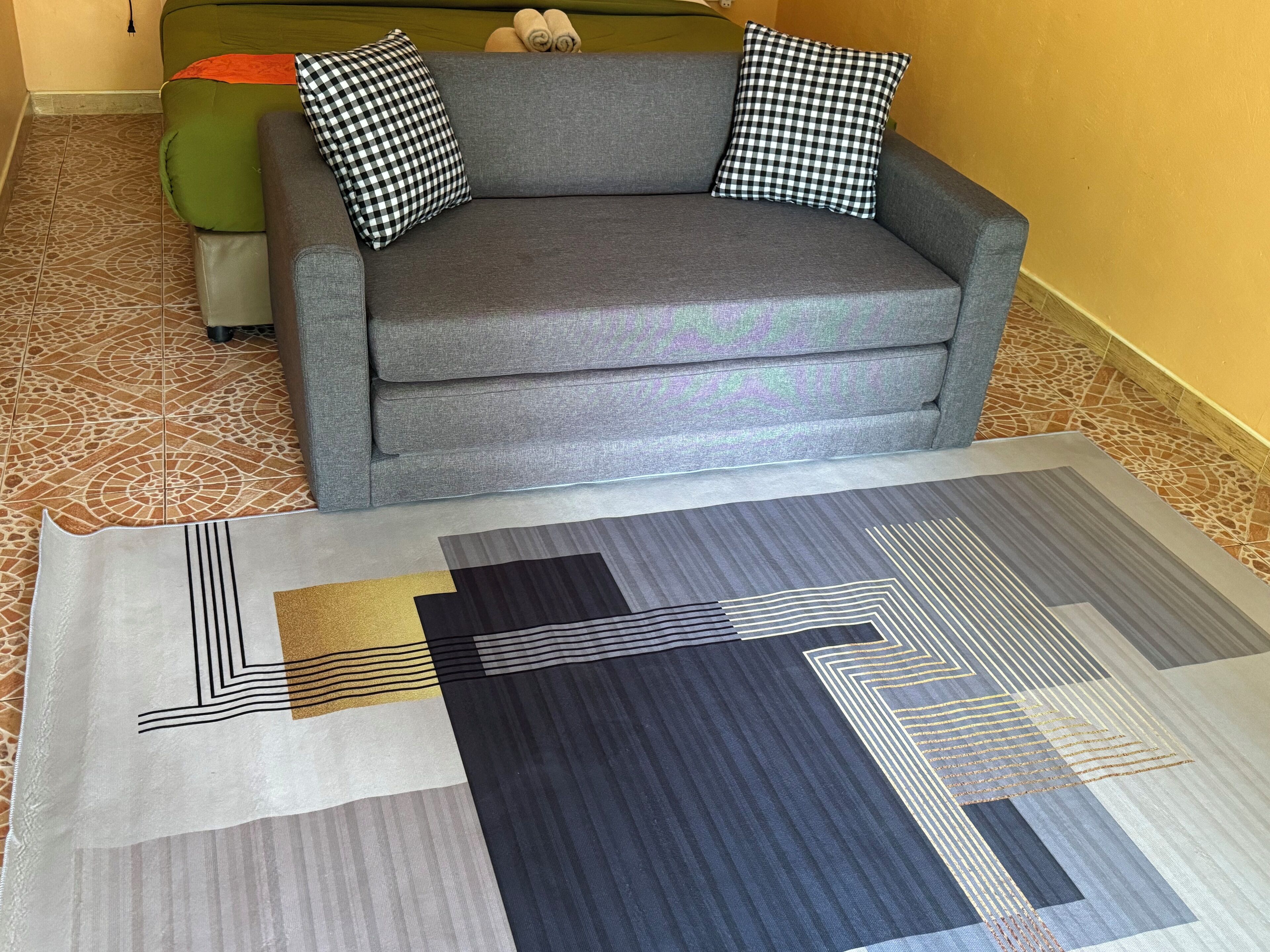 Un sofá gris con almohadones cuadriculados y una alfombra estampada con diseños geométricos.