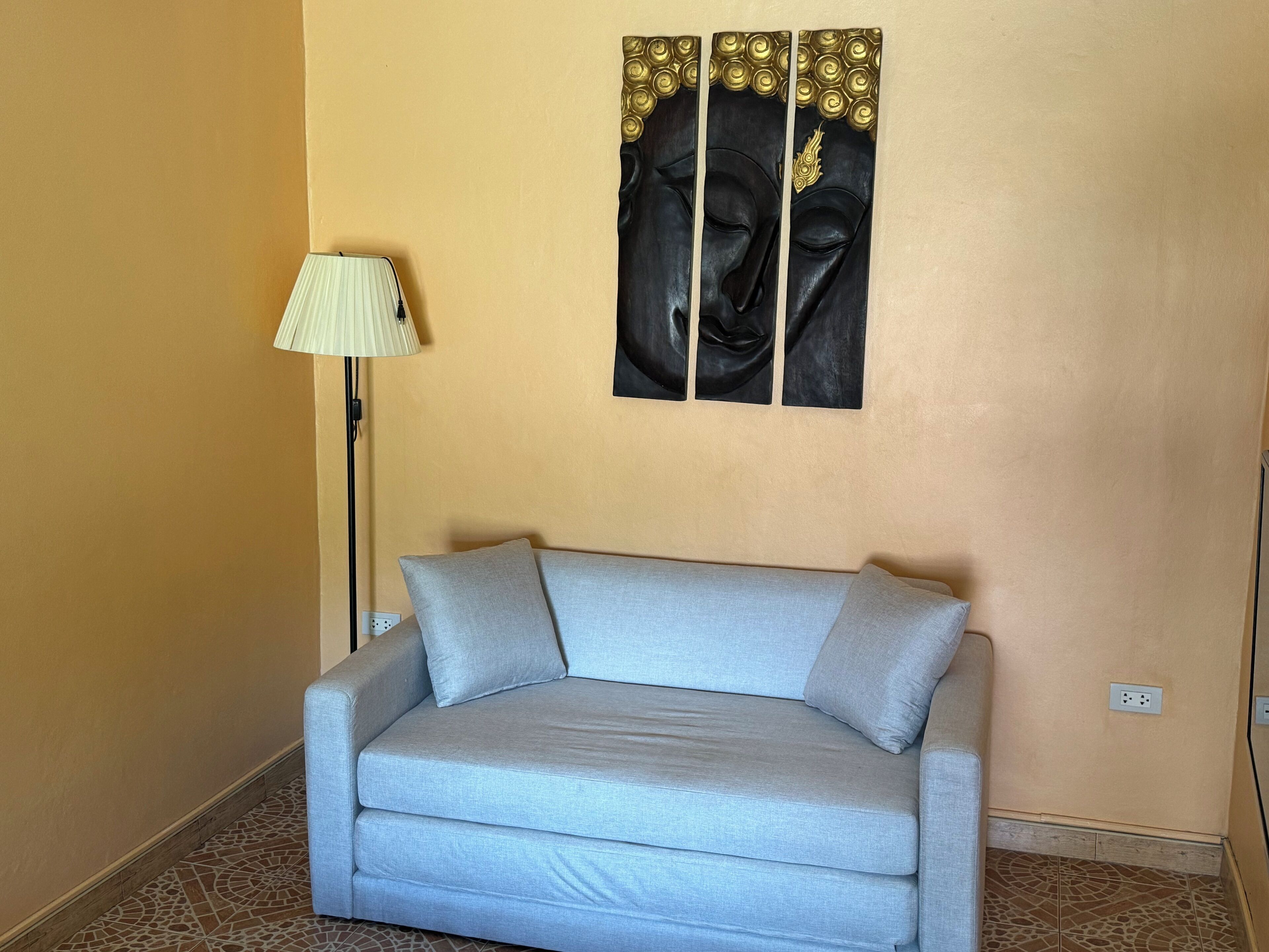 Una habitación con un sofá azul claro, una lámpara de pie y una obra de arte colgada en la pared que representa a Buda.