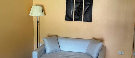 Una habitación con un sofá azul claro, una lámpara de pie y una obra de arte colgada en la pared que representa a Buda.