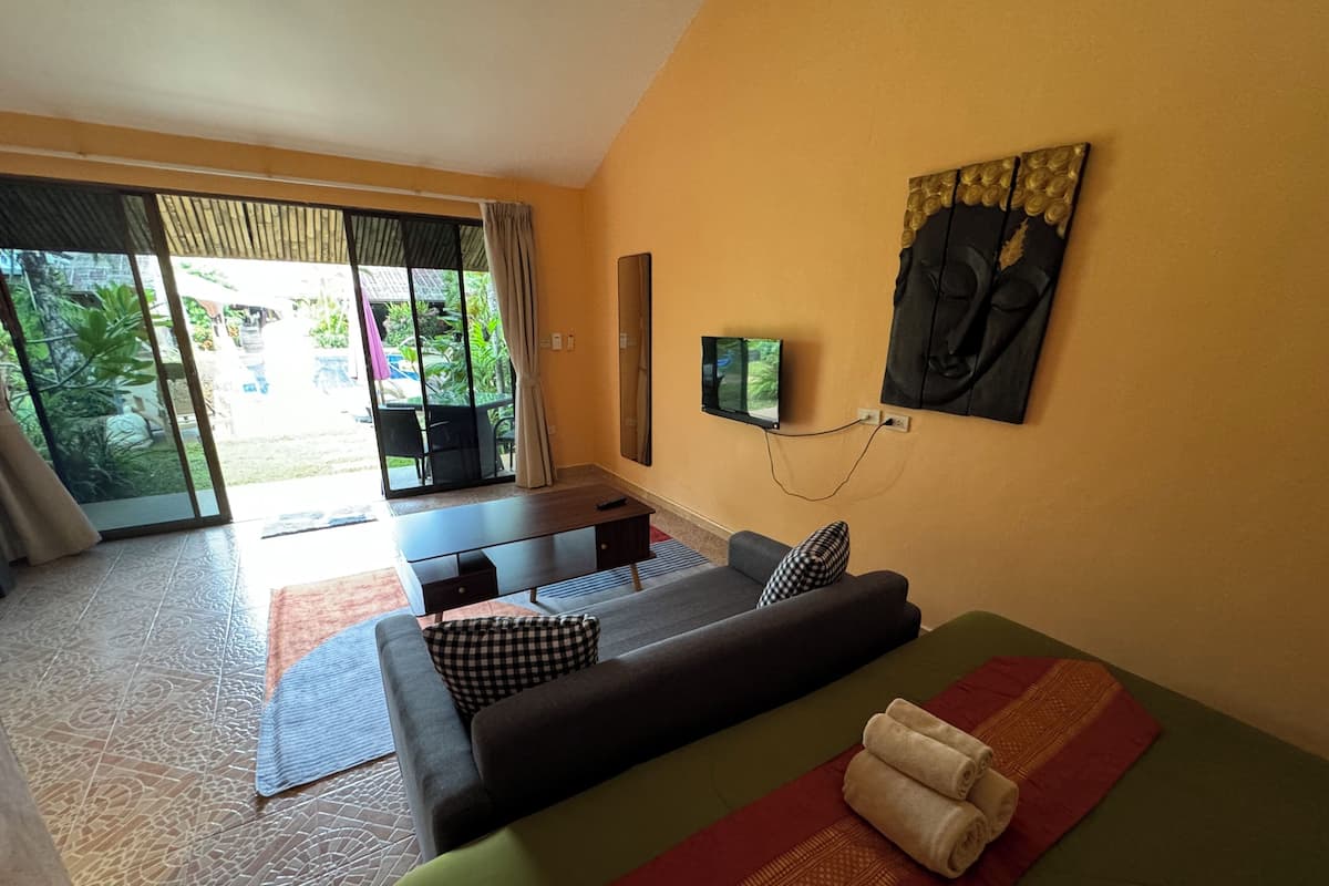 A room with a sofa, a TV mounted on the wall, and a sliding glass door leading to an outdoor area.