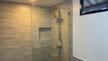 Un baño moderno con ducha envuelta en vidrio, estante empotrado y ventana sobre el lavabo.