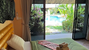 Une chambre d’hôtel avec un lit, des oreillers, une couverture verte, une serviette roulée et une vue sur une piscine extérieure et un jardin.