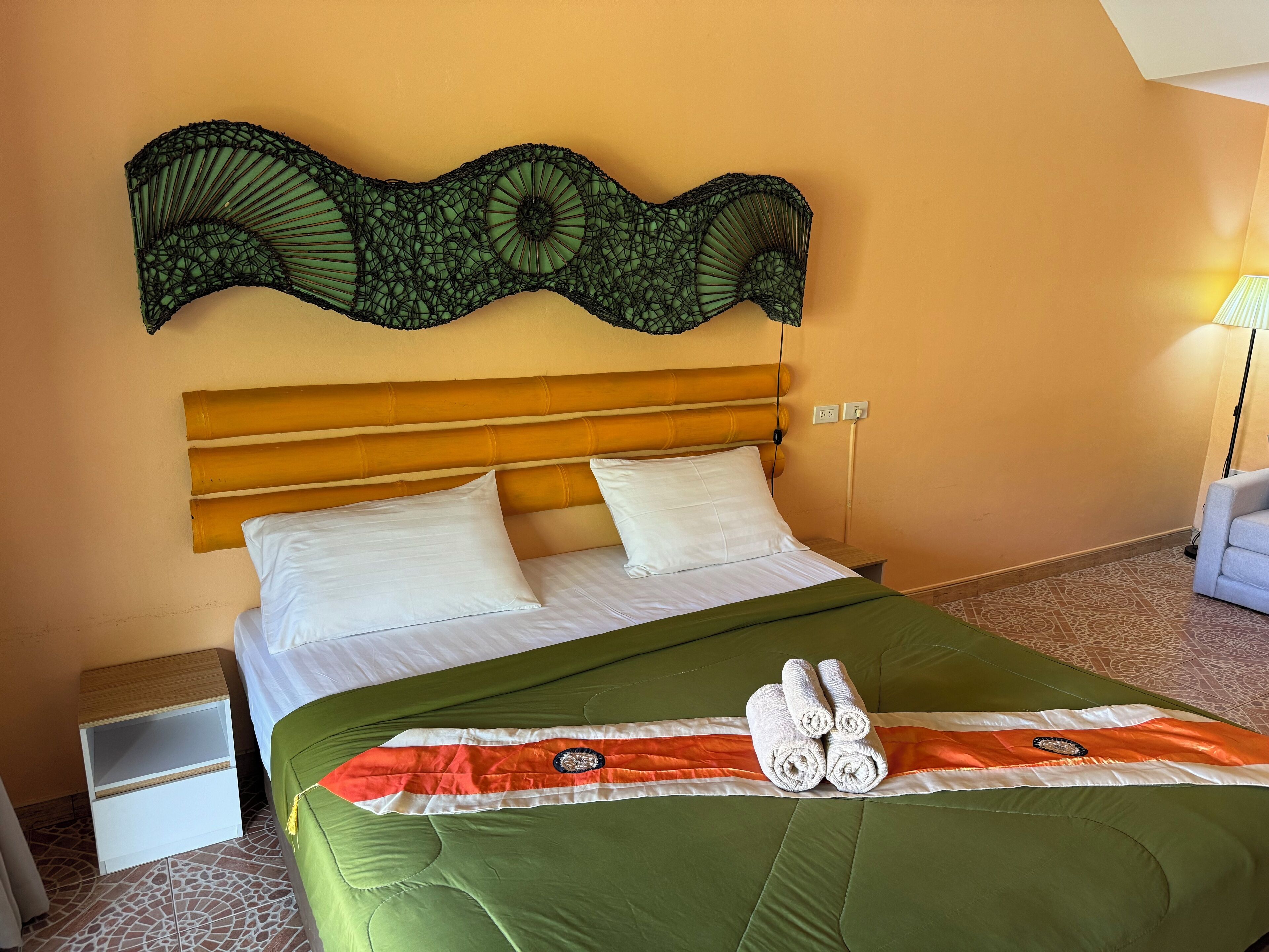 A neatly made bed with white linens, a green bedspread, and two rolled towels.