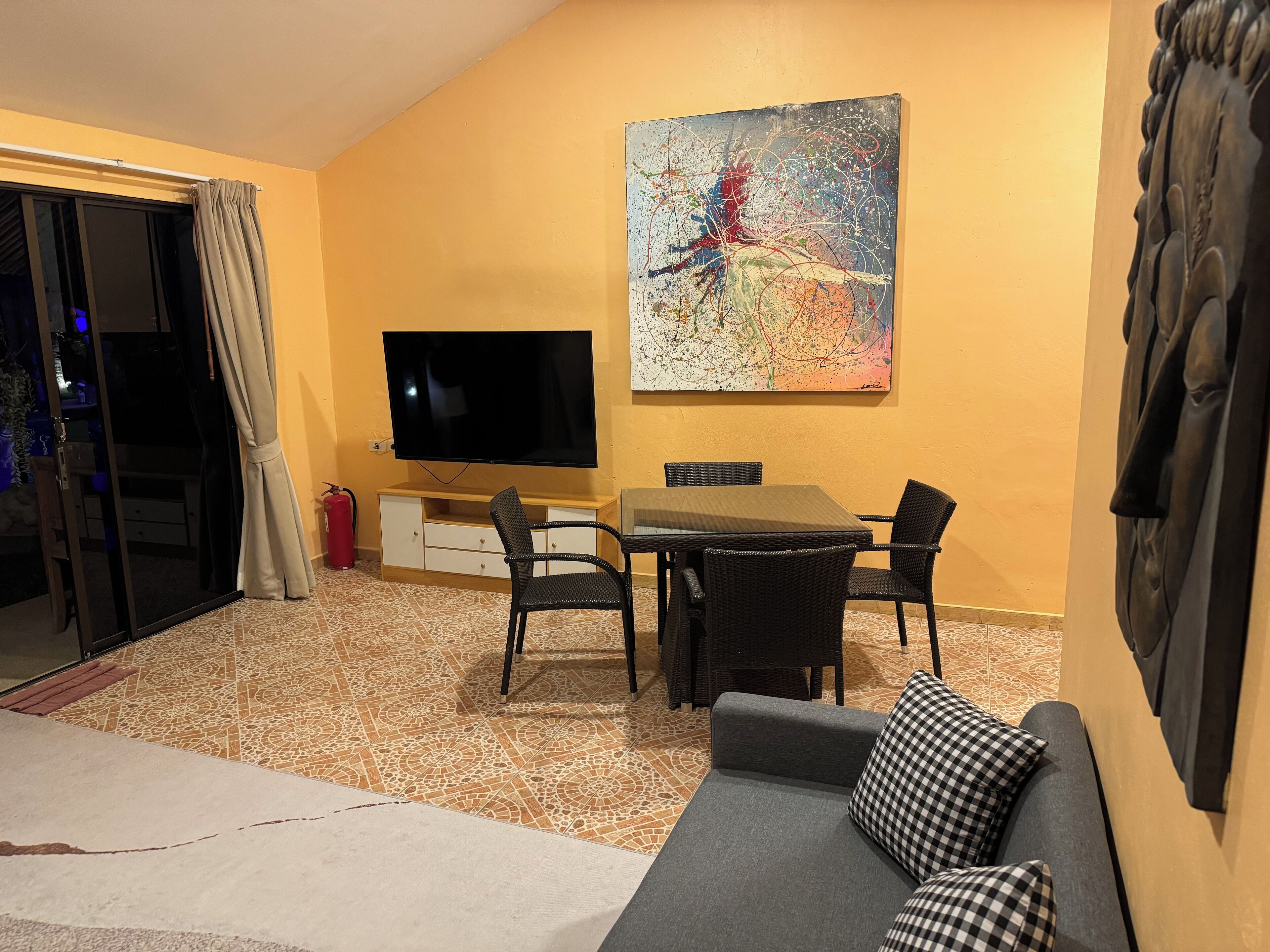 A living room with a flat-screen TV, a dining table with chairs, a sofa, and a large abstract painting on the wall.