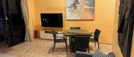 A living room with a flat-screen TV, a dining table with chairs, a sofa, and a large abstract painting on the wall.