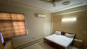 Un dormitorio con cama, ventilador de techo, equipo de aire acondicionado, mesita de noche y ventana con diseño floral.