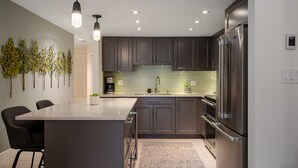 Une cuisine moderne avec des meubles de couleur sombre, des appareils en acier inoxydable et des luminaires suspendus.
