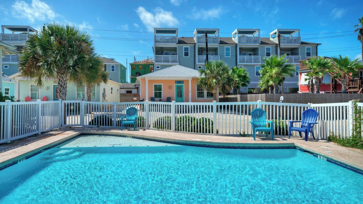 Een zwembad met stoelen, een witte omheining en meerhoogbouwwoningen op de achtergrond.