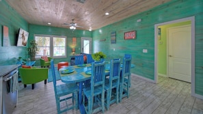 A dining area with a wooden ceiling, a ceiling fan, and a table with blue chairs. - Shared Pool, Walkable to Beach, Vibrant Beachy Design! Bay Bliss by Avantstay (Port Aransas)