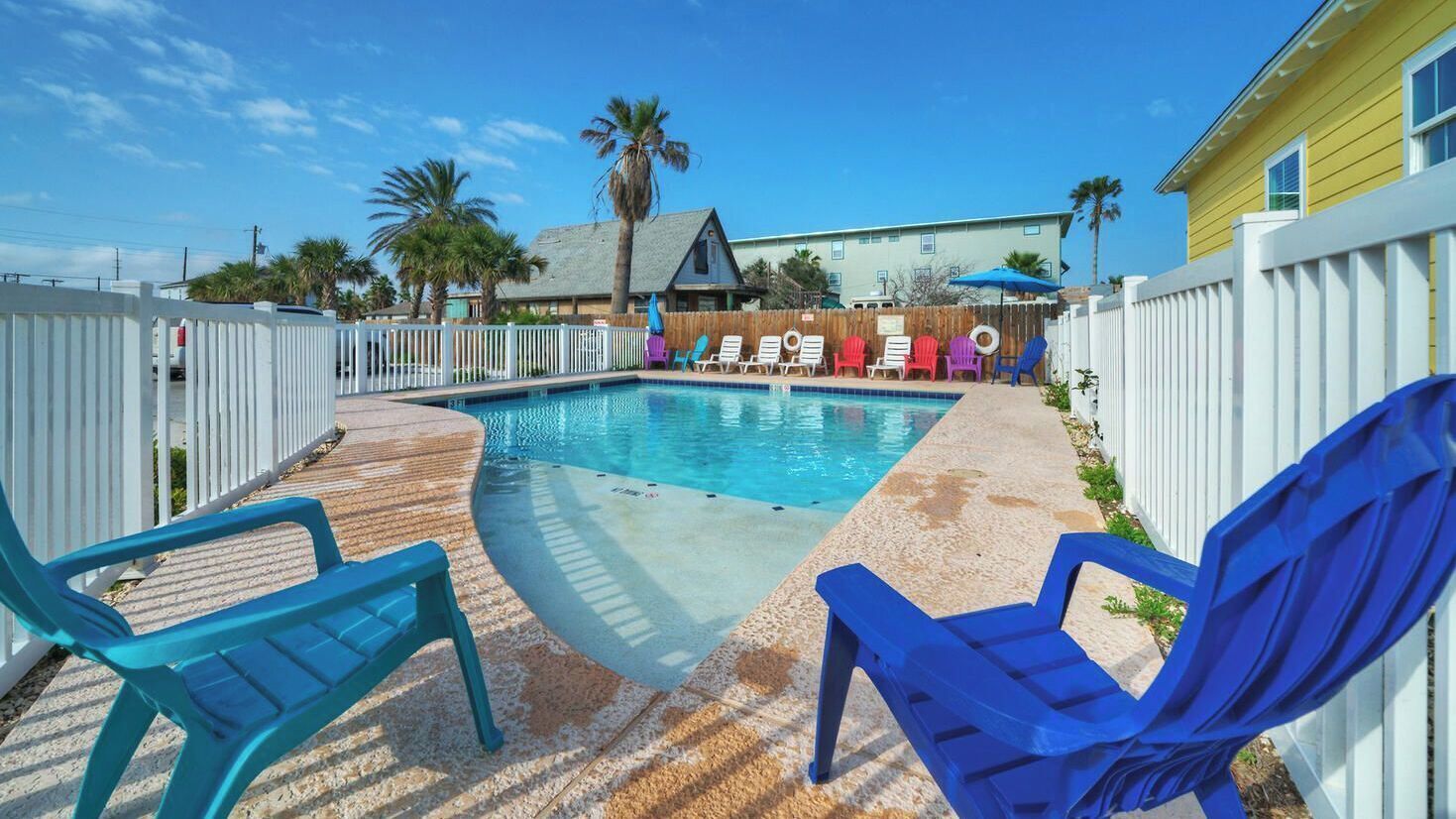 A swimming pool with lounge chairs, a wooden deck, and a fenced yard.