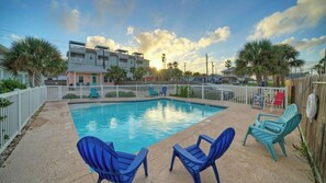 A swimming pool with blue chairs, a white fence, and a row of houses in the background. - Shared Pool, Walkable to Beach, Vibrant Beachy Design! Bay Bliss by Avantstay (Port Aransas)