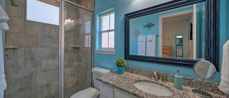 A bathroom with a glass shower enclosure, a white toilet, a granite countertop with a sink, and a large mirror.