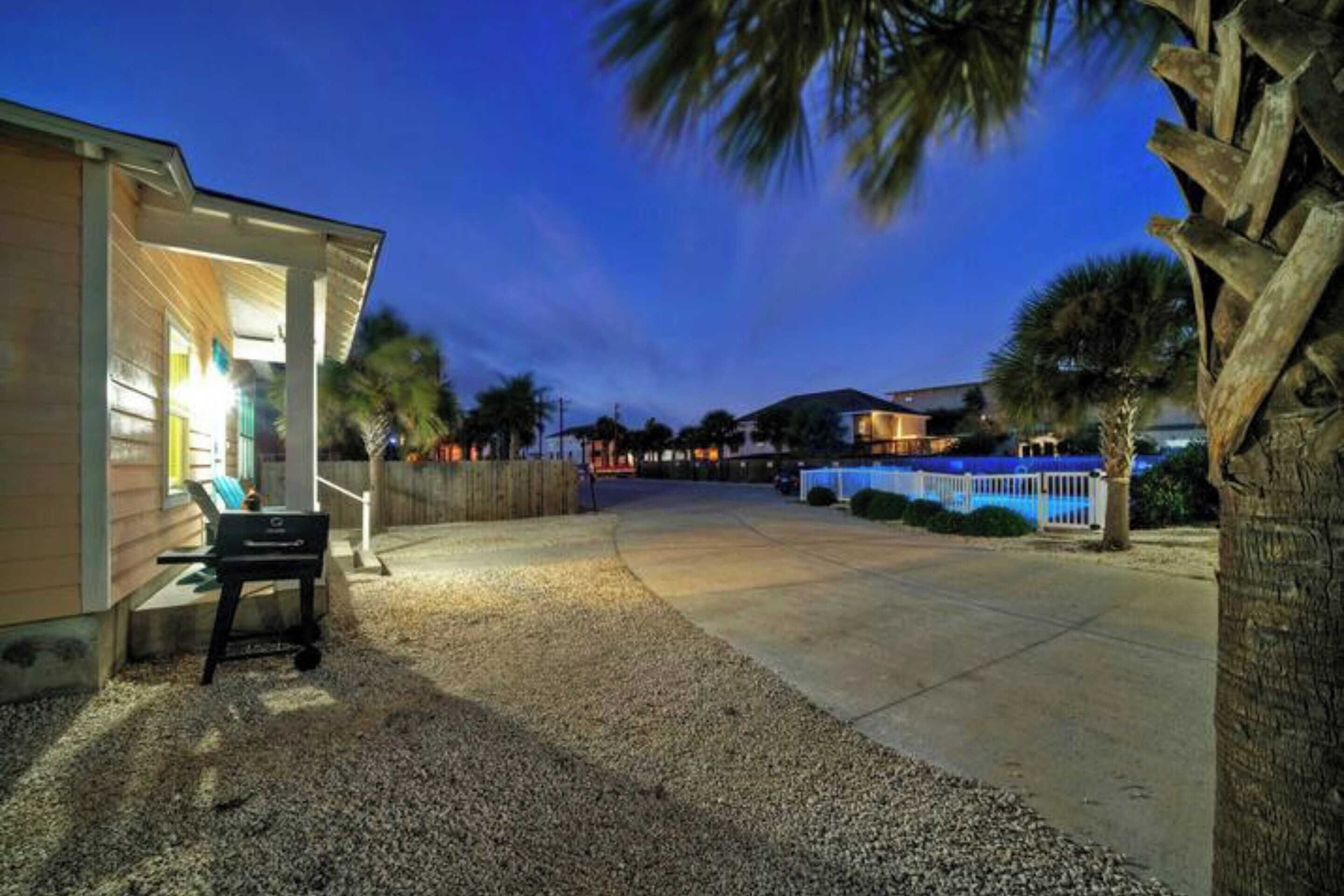 A residential property with a covered patio, gravel driveway, and palm trees.