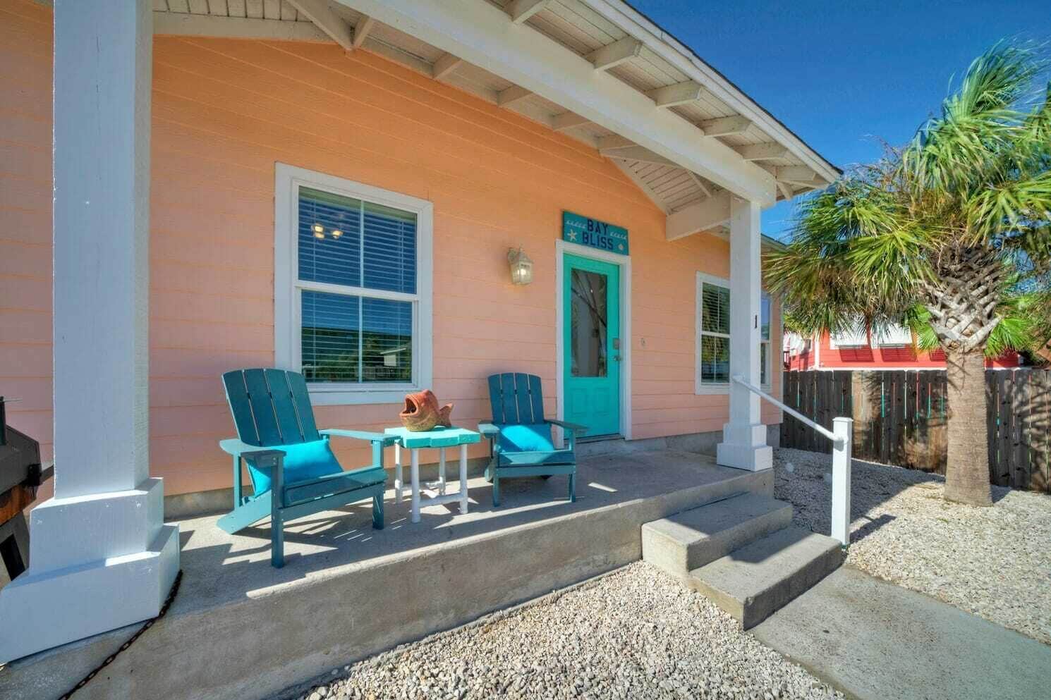 A house with a porch, two turquoise chairs, a small table, and a turquoise door.