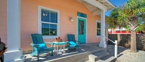 A house with a porch, two turquoise chairs, a small table, and a turquoise door.