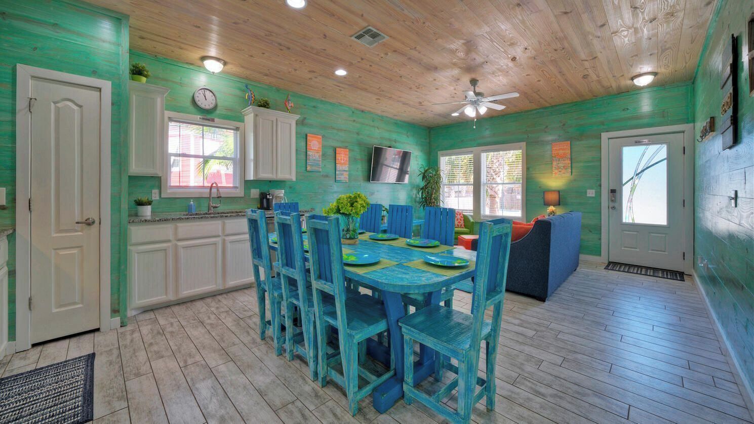 A kitchen with teal walls, white cabinets, a dining table with blue chairs, and a ceiling fan.