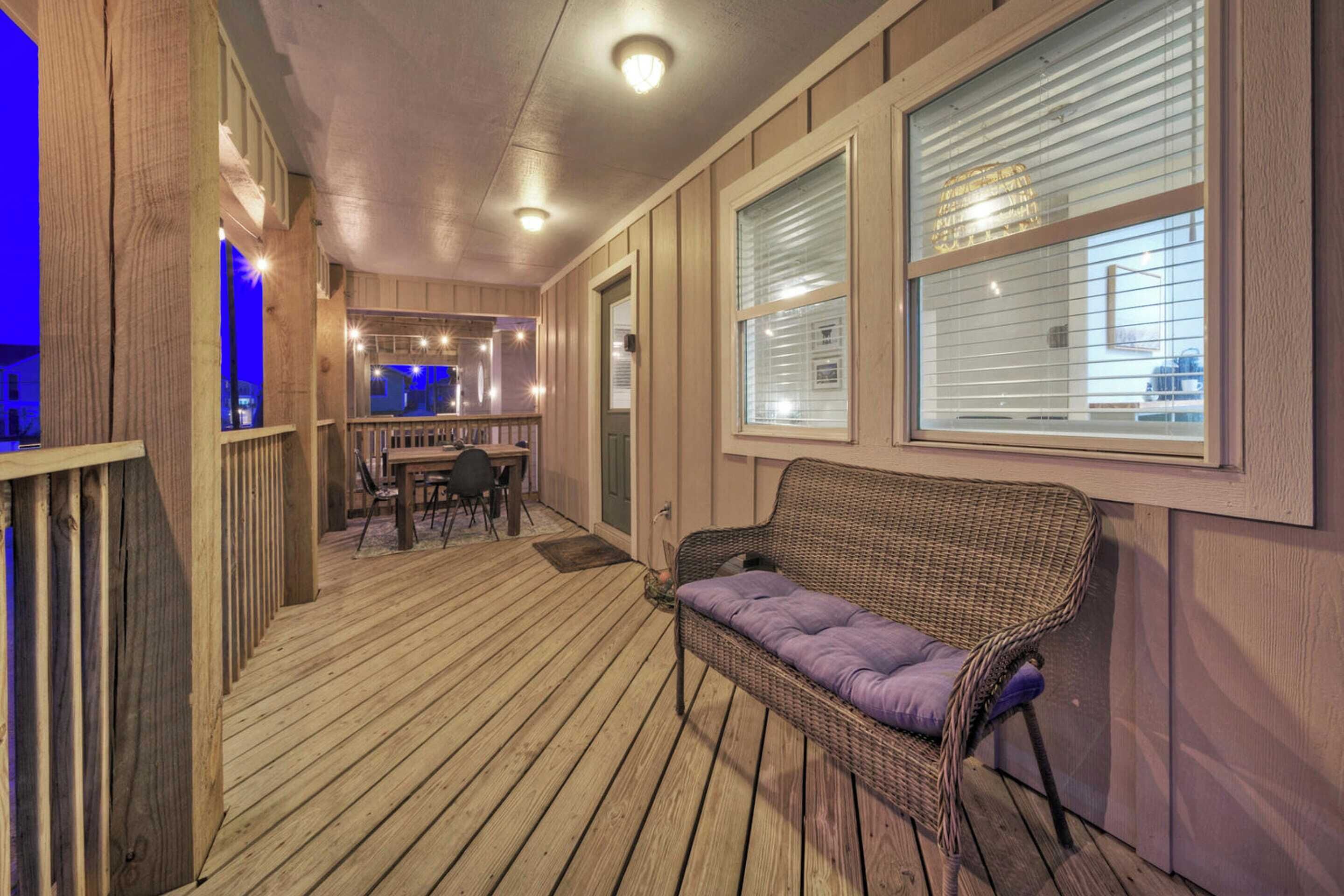 A covered porch with a wicker sofa, wooden deck, and a dining area with chairs and a table.