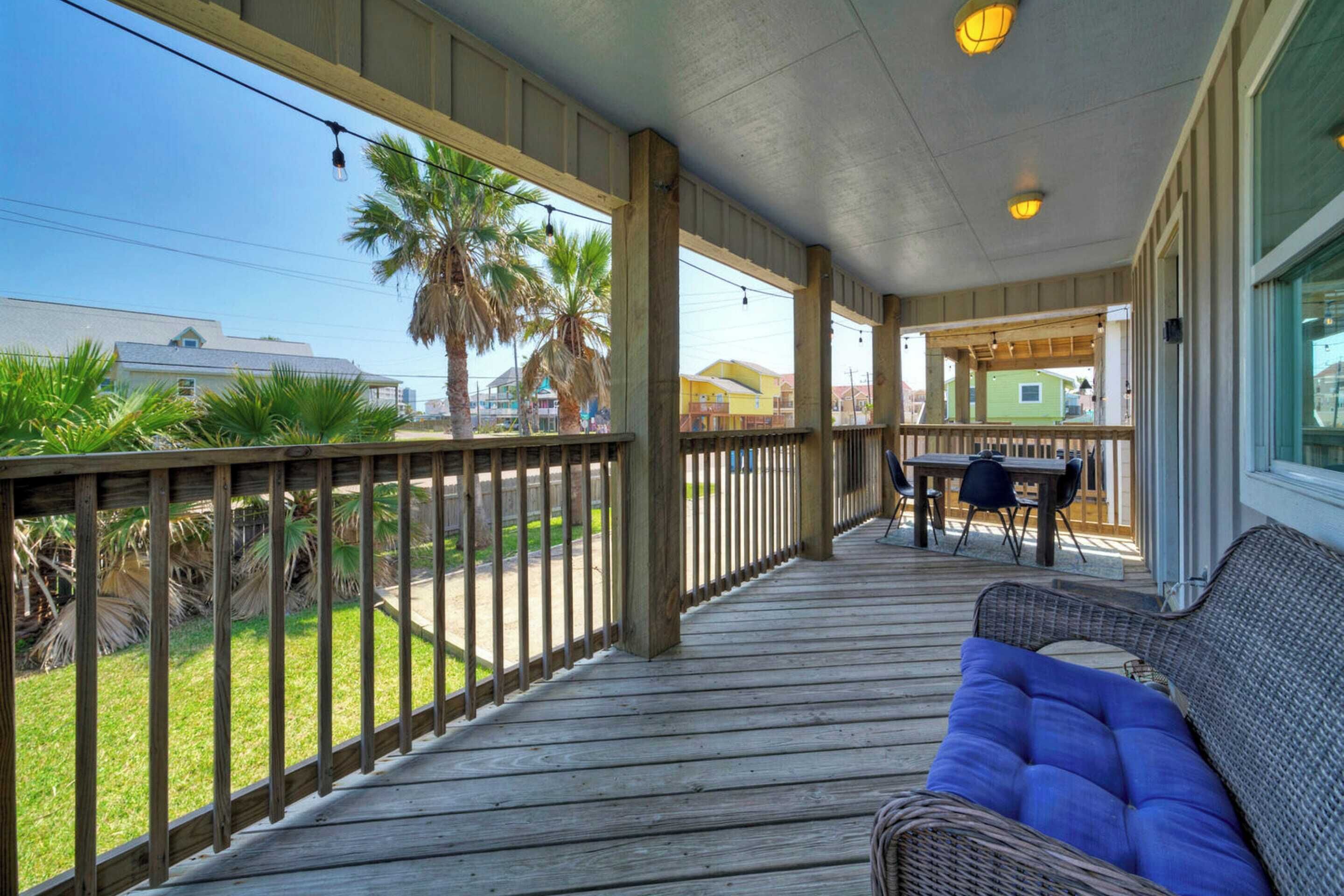A covered outdoor area with a wooden deck, a wicker sofa, and a table with chairs.