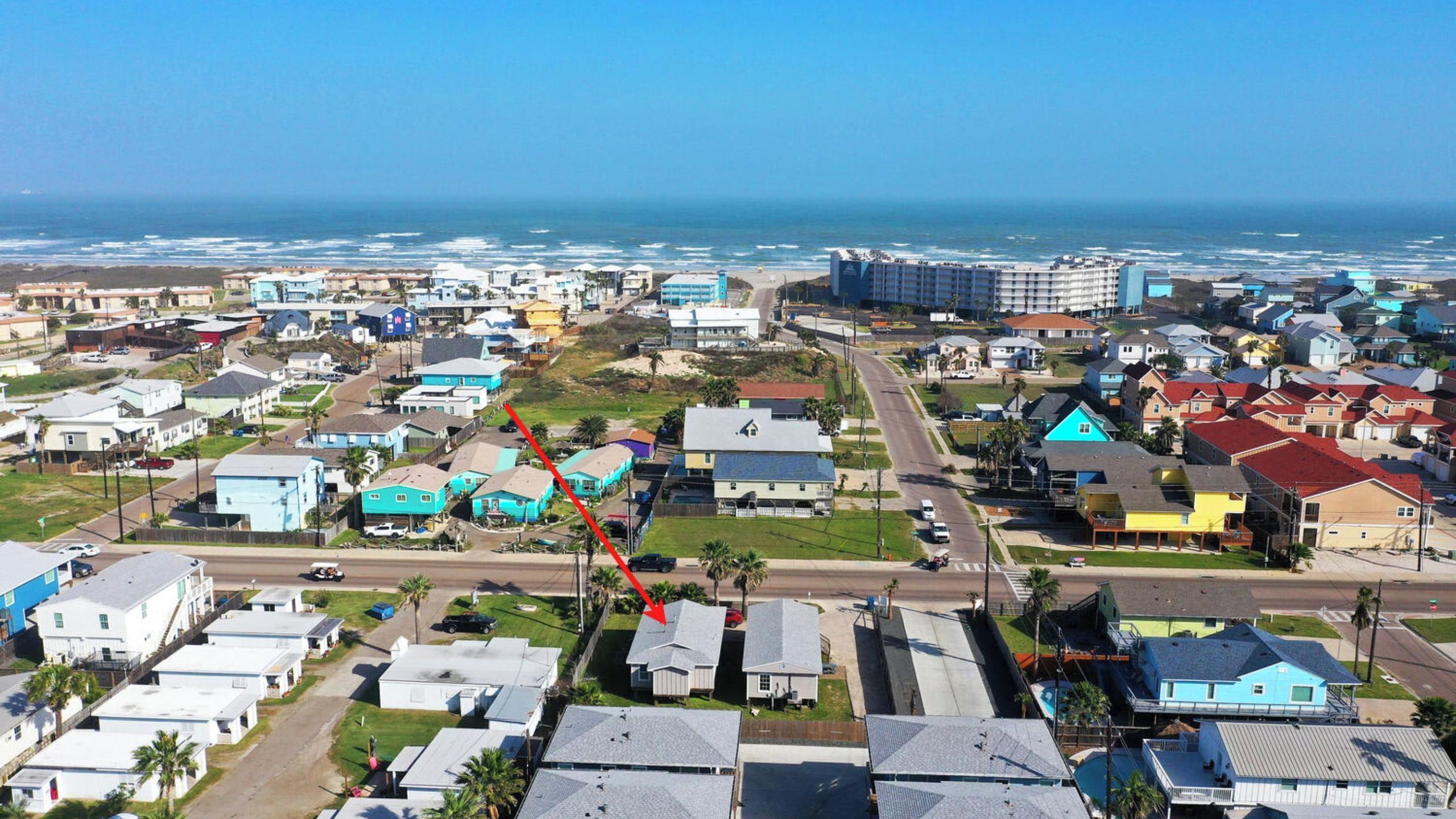 A coastal residential area with houses, a road, and a beach in the background.