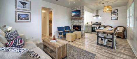 Una sala moderna con sofá, mesa de centro y sillas azules, una cocina con estufa y microondas, y un comedor con mesa y sillas.