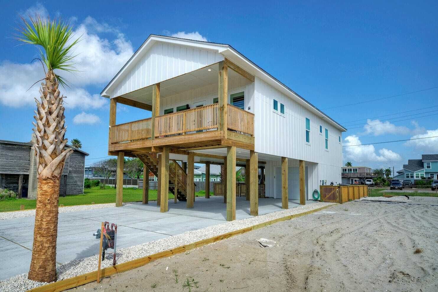 A two-story house with a balcony, wooden deck, and a palm tree in the foreground.