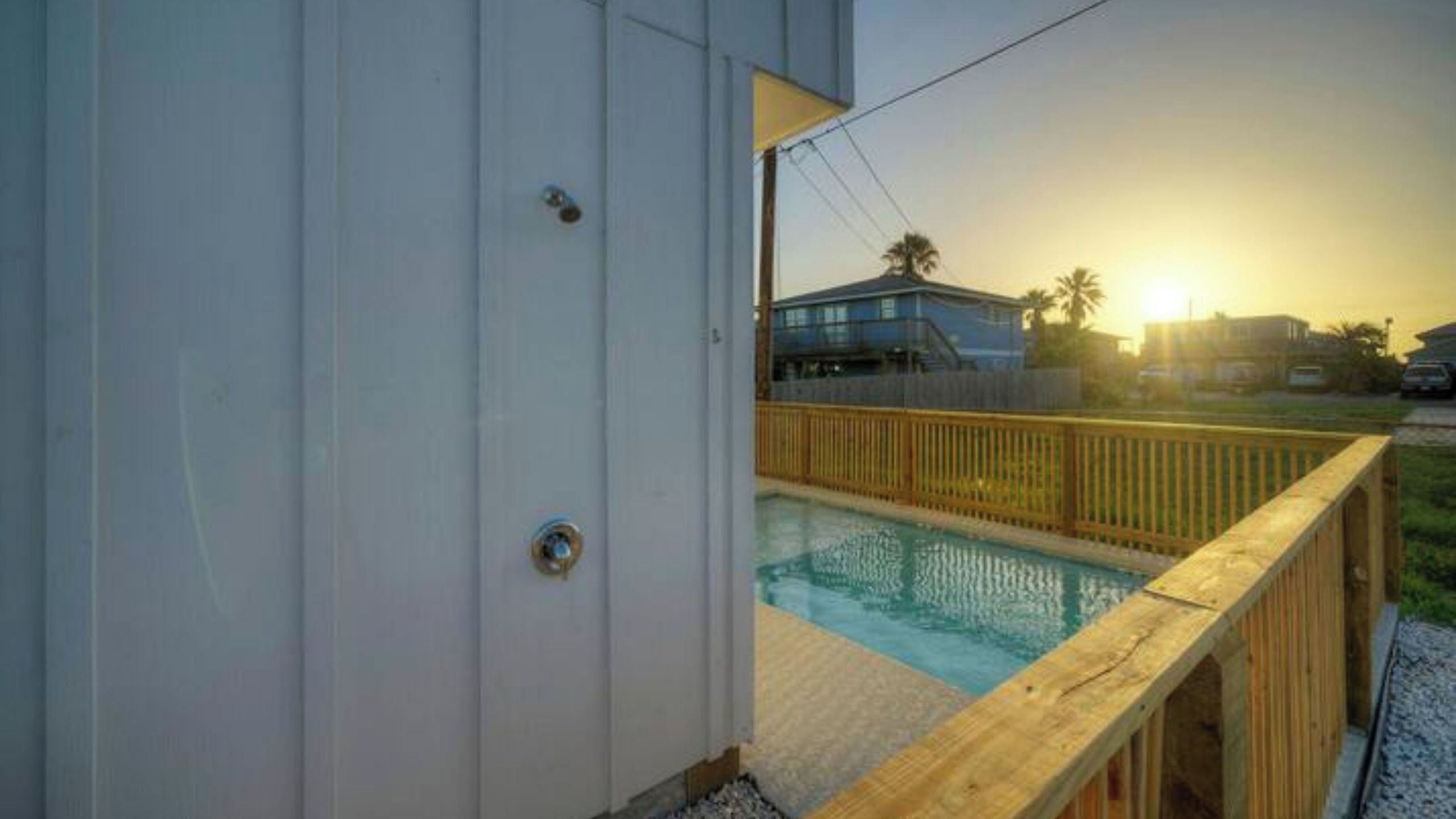A pool with a wooden deck, a white building, and a sunset in the background.