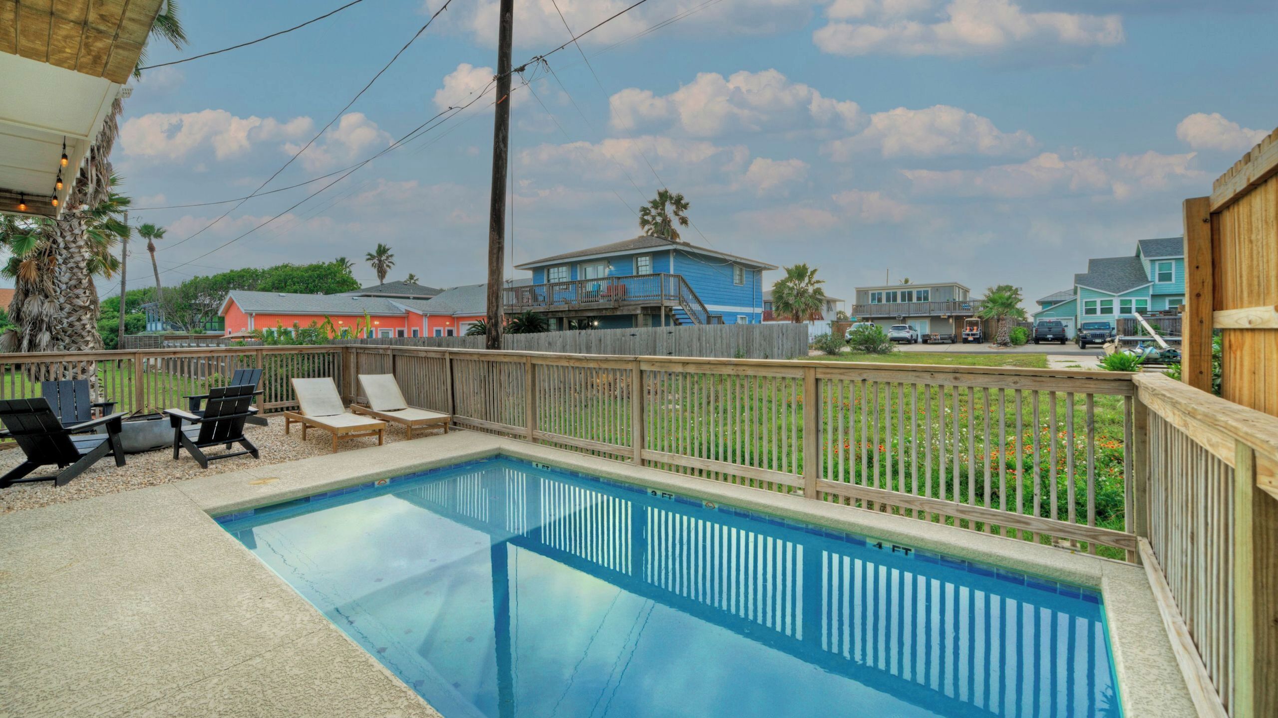 A swimming pool with a wooden deck and lounge chairs, surrounded by a wooden fence.
