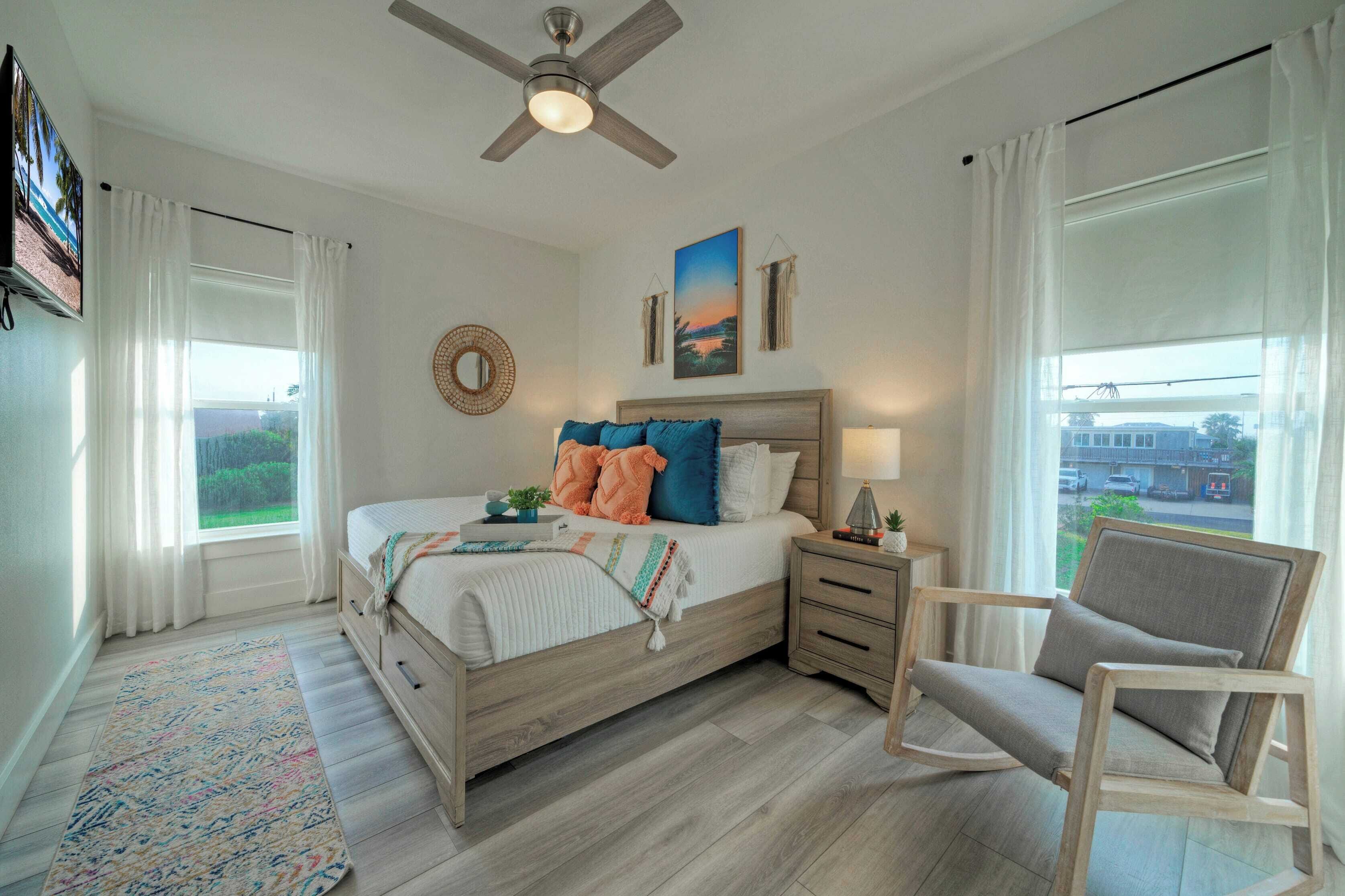 A bedroom with a bed, bedside tables, a chair, a ceiling fan, and a window with curtains.