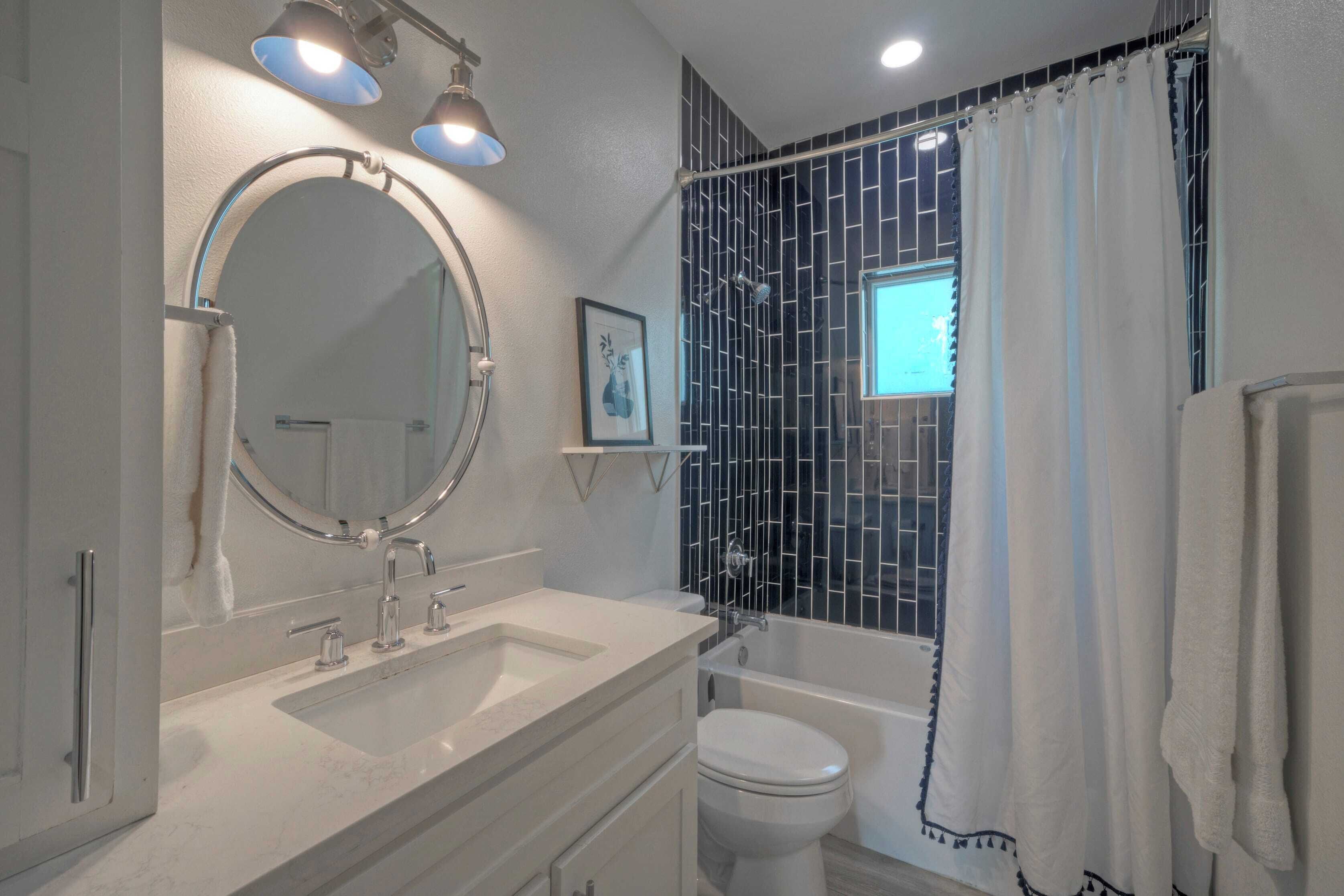 A bathroom with a white sink, a round mirror, a toilet, and a bathtub.