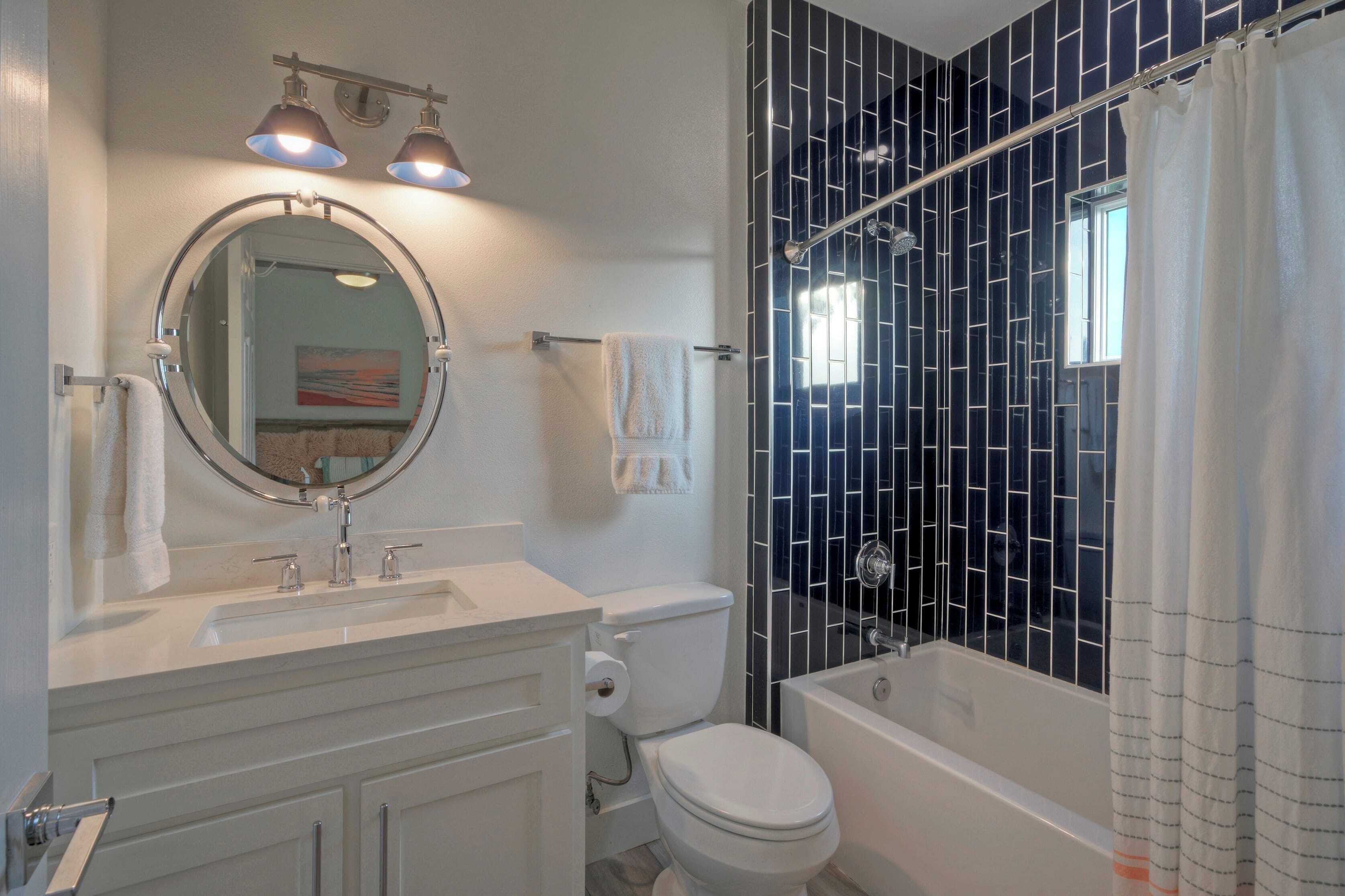 A modern bathroom with a white vanity, a round mirror, a toilet, and a bathtub.