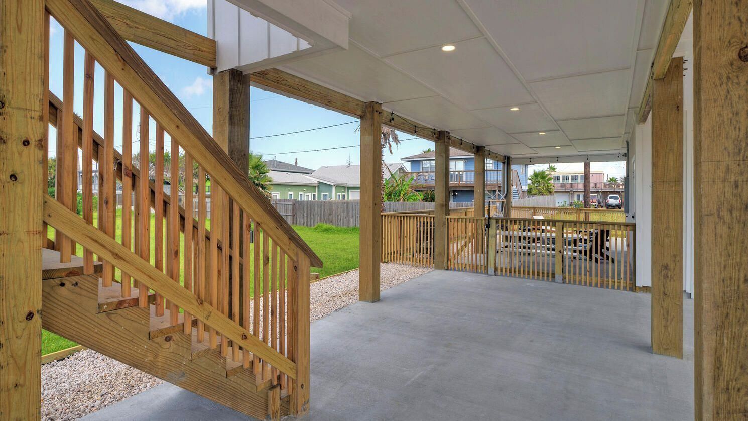Un espacio al aire libre cubierto con una escalera de madera, piso de concreto y vista a edificios residenciales.