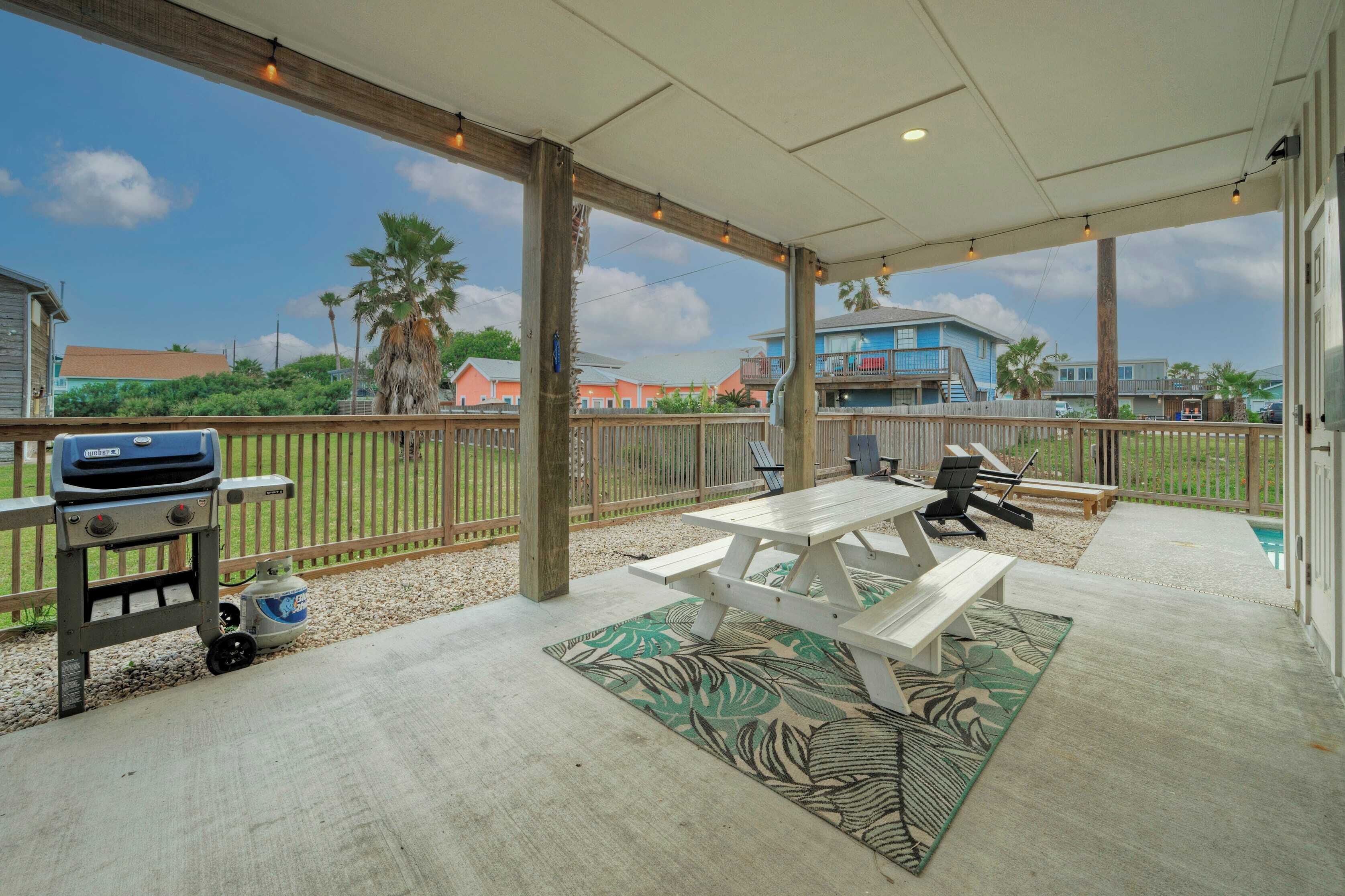 An outdoor patio with a grill, picnic table, and lounge chairs.