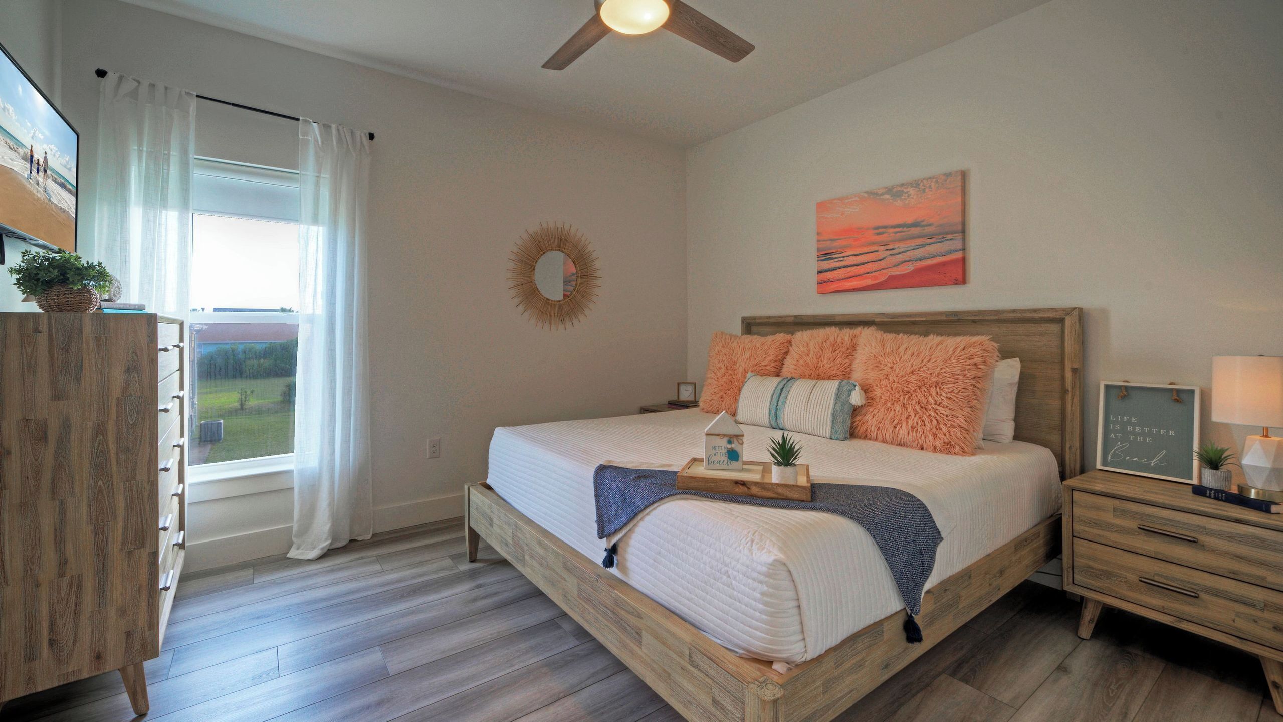 A bedroom with a bed, a wooden dresser, a nightstand, a ceiling fan, and a view of the outdoors.