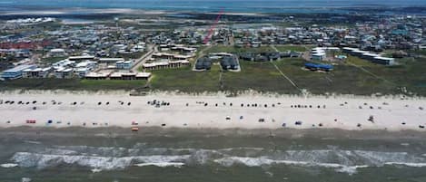 An aerial view of a coastal area with a beach, buildings, and a road.