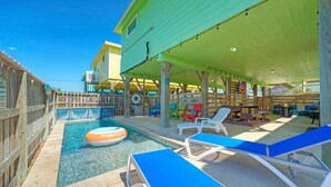 Un espace piscine équipé de chaises longues, d’un flotteur et d’un patio couvert avec des tables et des chaises.