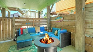 Une terrasse extérieure avec un foyer, des meubles en osier et une clôture en bois.