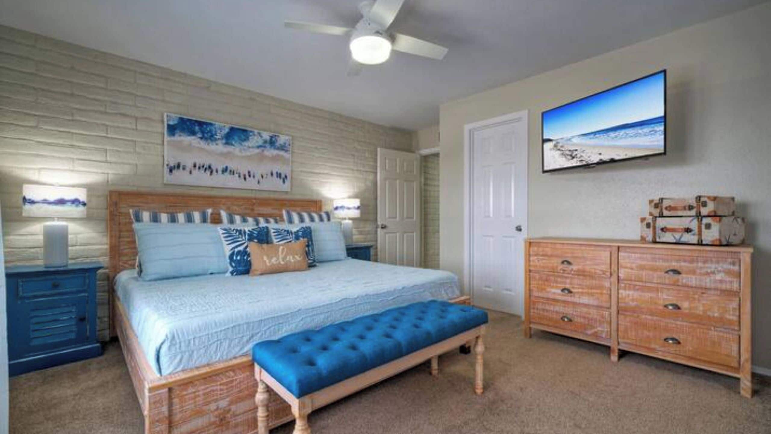 A bedroom with a bed, a bench, a dresser, a television, and a ceiling fan.